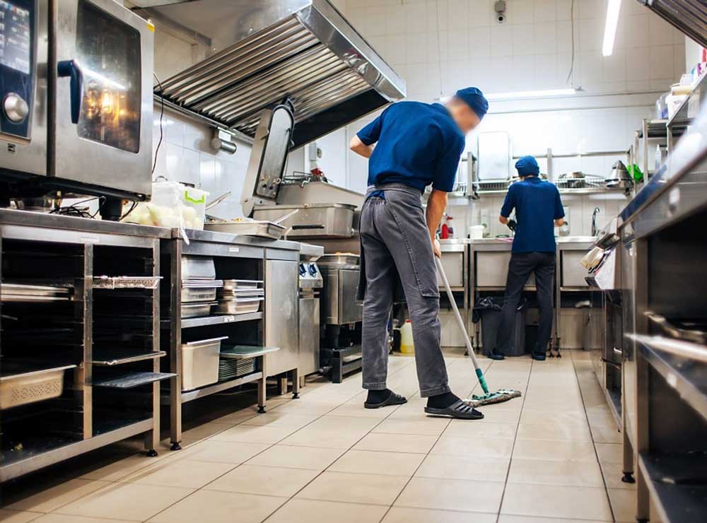 Technician deep cleaning behind commercial kitchen equipment